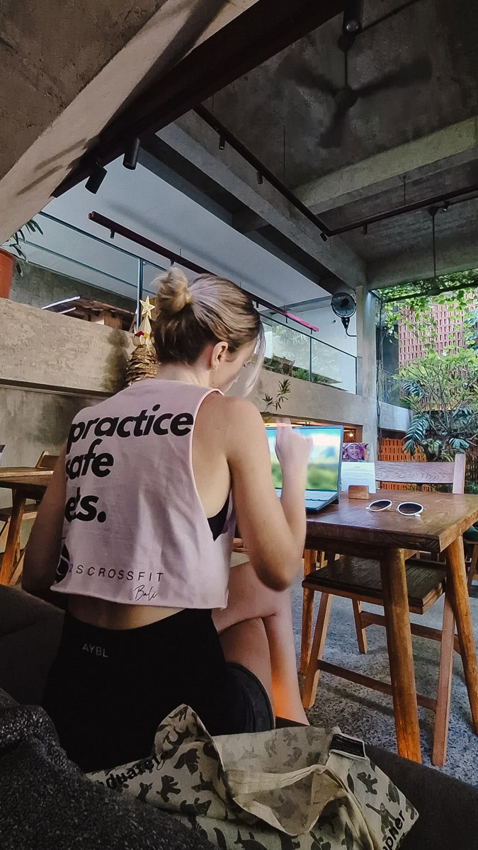What To Wear In Bali - Outfit Ideas & Bali Packing Guide 11 Jodie working in a cafe in Canggu wearing gym clothing, including a pink crop top from a Crossfit box, and with her hair tied in a messy bun.