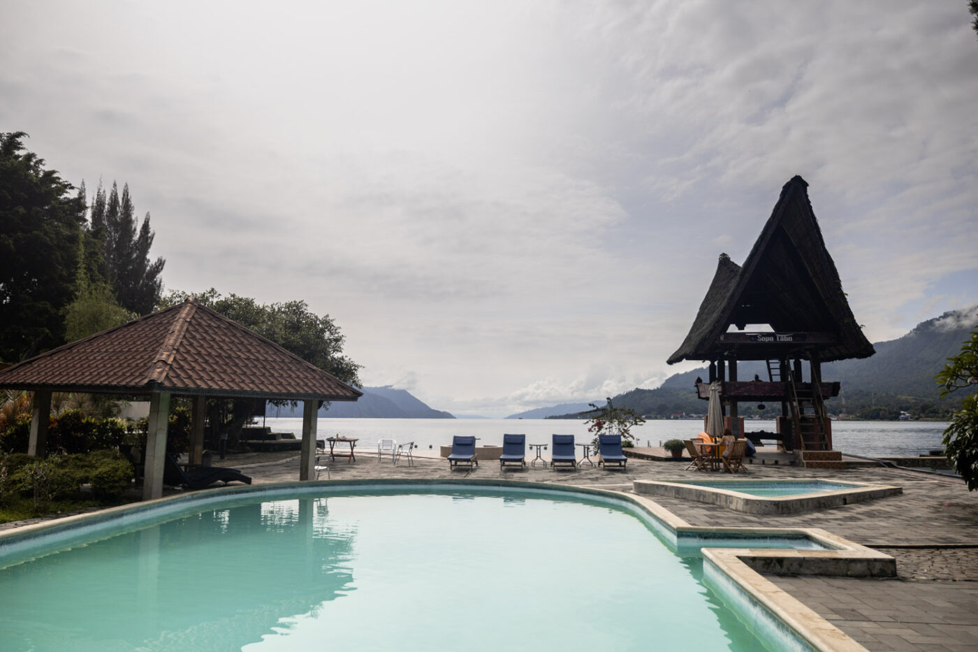 A Unique Stay At Tabo Cottages, Samosir Island: A Lake Toba hotel with a story 15 A view of the outdoor pool at Tabo Cottages with Lake Toba and a Batak house in the background