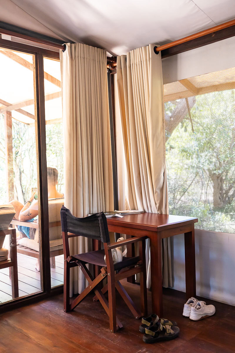 Wild Trails Yala by Suri: A Sustainable Tented Safari Camp Experience on the Edge of Yala National Park, Sri Lanka 9 A desk and chair at Wild Trails Yala by Suri. Outside the window, you can see a man relaxing on a chair on the deck.