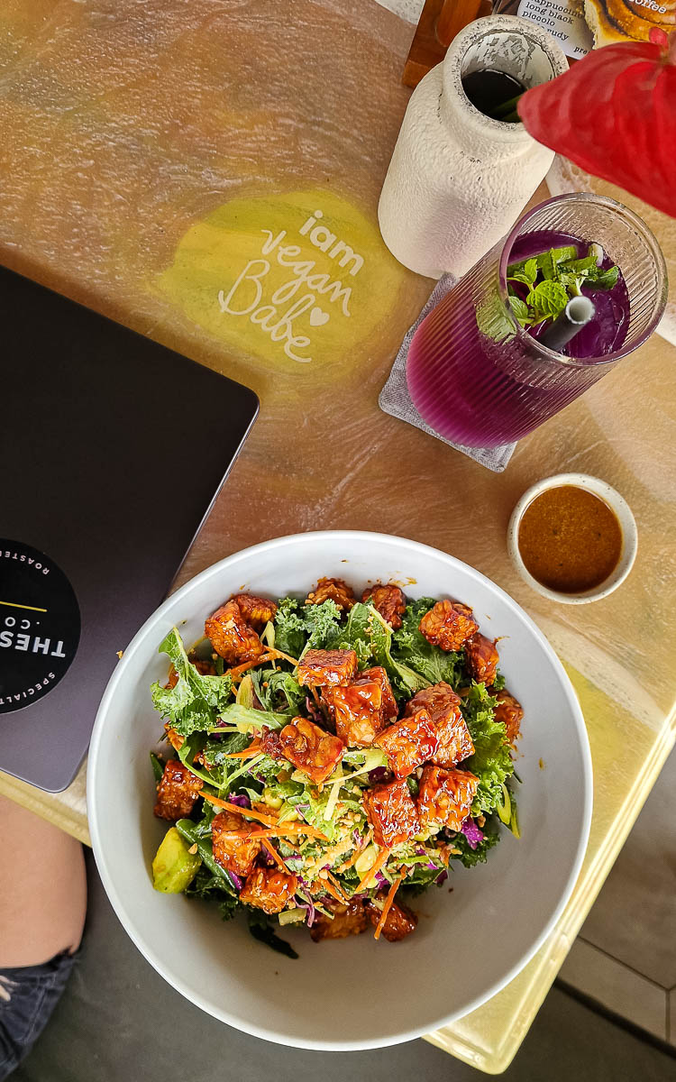 Vegan Canggu: A tried-and-tested guide to vegan cafes & restaurants in Bali's digital nomad hotspot 9 A top down view with big bowl of vegan salad, a purple drink and a closed laptop at I Am Vegan Babe in Canggu