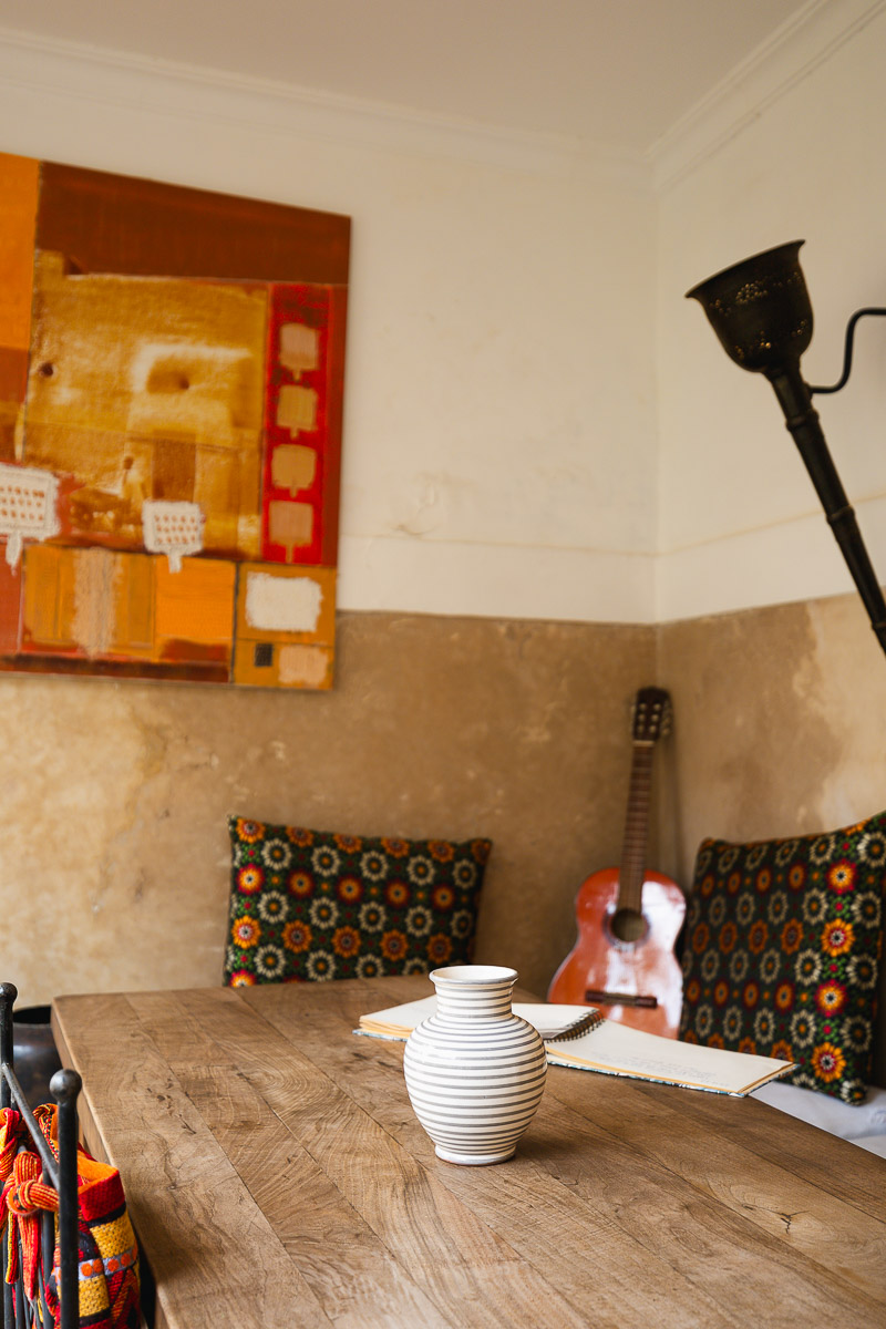 Riad Bamileke (Medina Marrakech): Complete Review & FREE Morocco Travel Guide 7 A wooden table with a ceramic on top. There are chairs with African print fabric around in Riad Bamileke in Marrakech