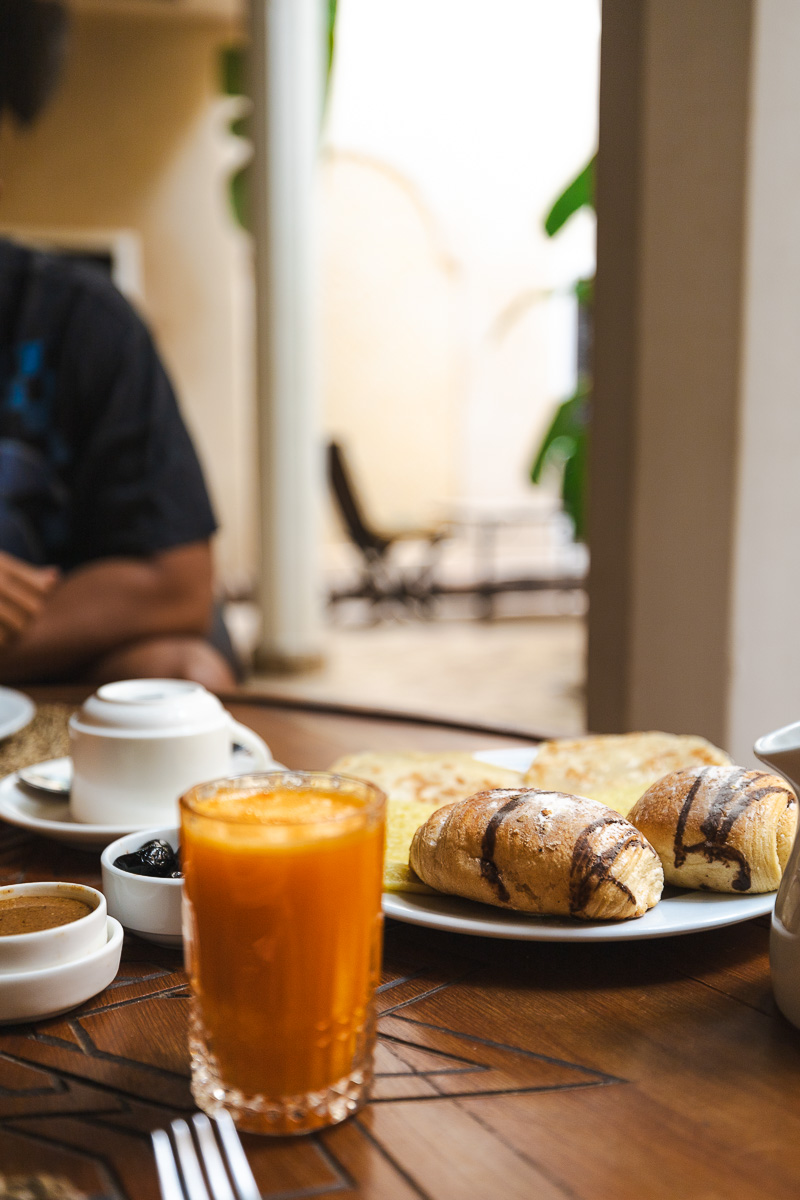 Riad Bamileke (Medina Marrakech): Complete Review & FREE Morocco Travel Guide 8 An orange coloured juice and fresh pastries on a table inside a riad courtyard