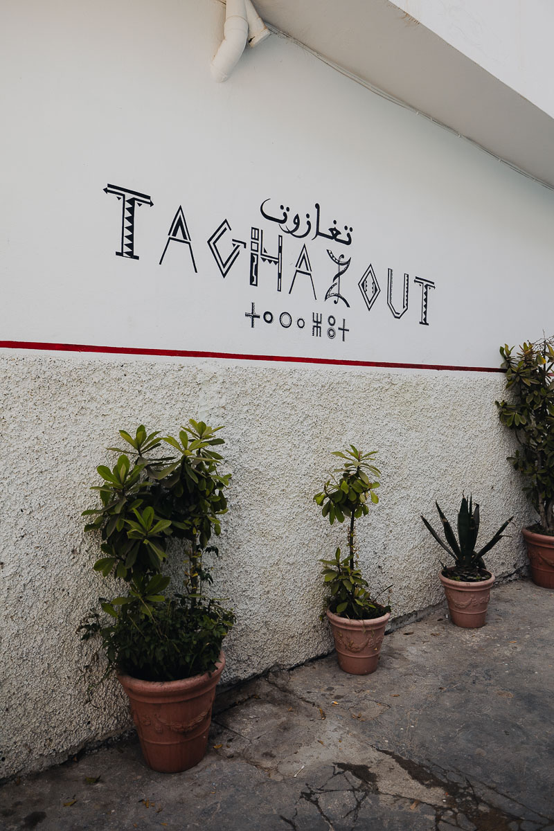 Taghazout Travel Guide 1 A white wall with Taghazout written in English, Berber and Arabic, with plants below