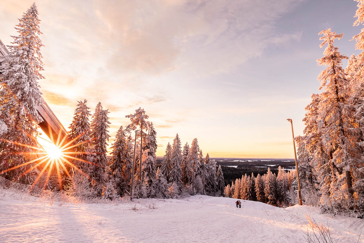 Sunset with a sun star shining through snow capped trees in front of a ski jump at Puijo Peak in Kuopio Finland